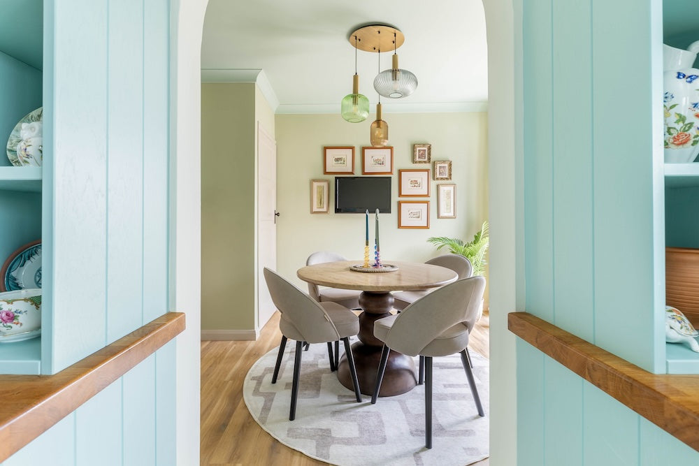 Dining area with round table and chairs, framed pictures on the wall, and light blue walls.