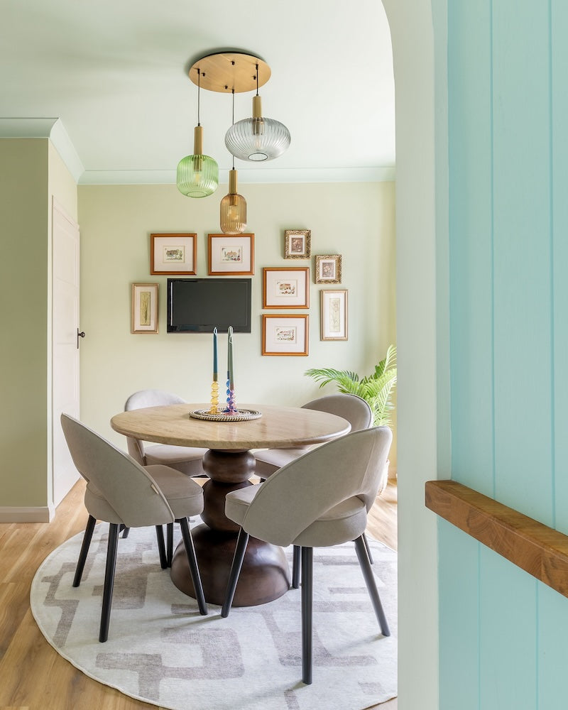Dining room with round table and chairs, framed pictures on the wall, and a television with green walls and ceiling.