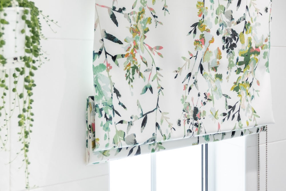 Floral patterned roman blind on a bathroom window with a white tiled wall background.