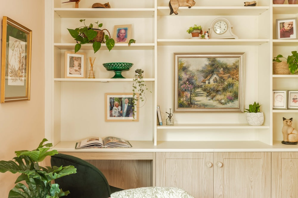 Decorative wall unit with books, plants, and framed pictures in a home setting.