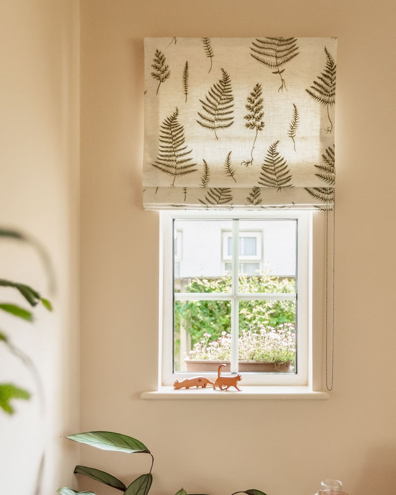 Window with a roman blind featuring fern patterns on a beige wall.